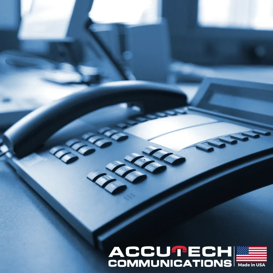 Close-up of a dark multi-line desk phone handset and keypad in a blue-tinted office