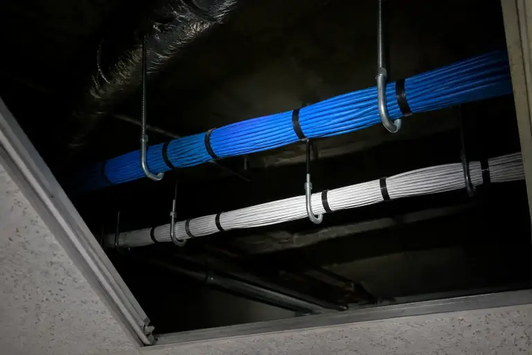 Flashlight lighting J-hooks carrying neat cable bundles above a lifted office ceiling tile