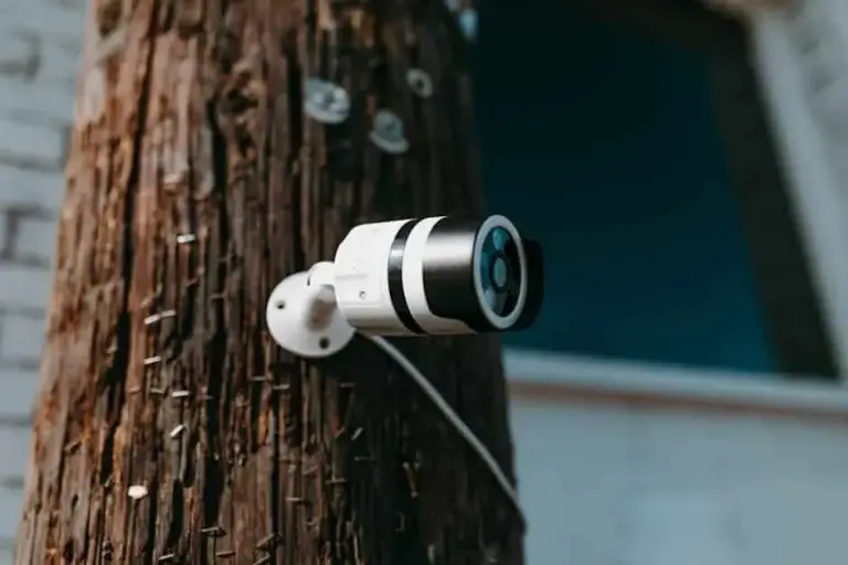 White bullet security camera mounted on a weathered wooden utility pole beside a building