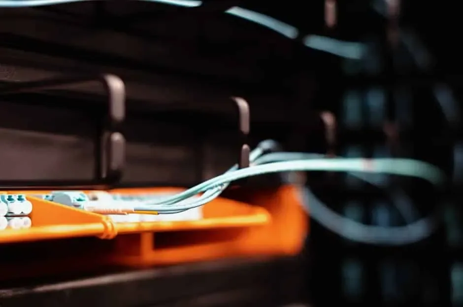 Aqua fiber jumpers feeding into an orange fiber splice tray inside a dark equipment rack
