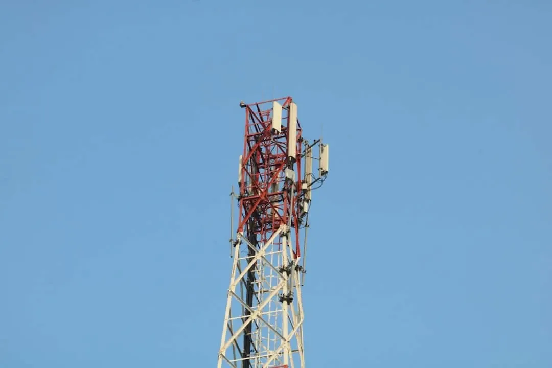 Red and white cellular tower with antenna panels against a clear blue sky