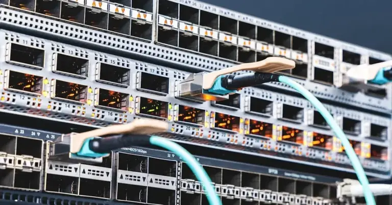Aqua fiber cables plugged into optical ports on a rack-mounted switch with amber port lights