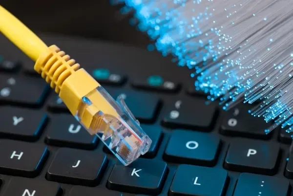 Yellow Ethernet plug resting on a laptop keyboard beside a bundle of glowing fiber strands