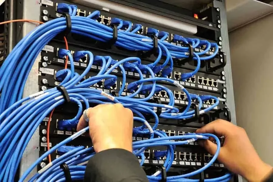 Hands plugging blue patch cords into a rack patch panel lined with cable management rings