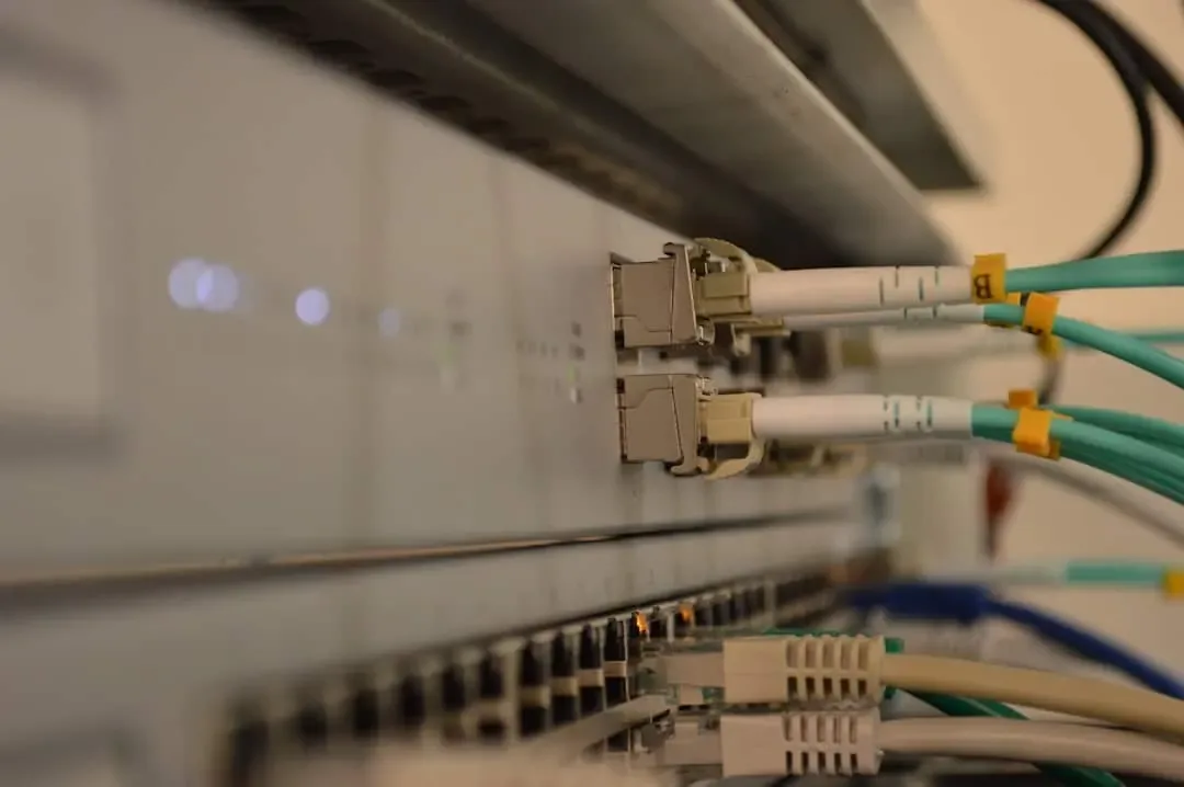Aqua fiber patch cords with labeled connectors plugged into a switch above gray copper cables