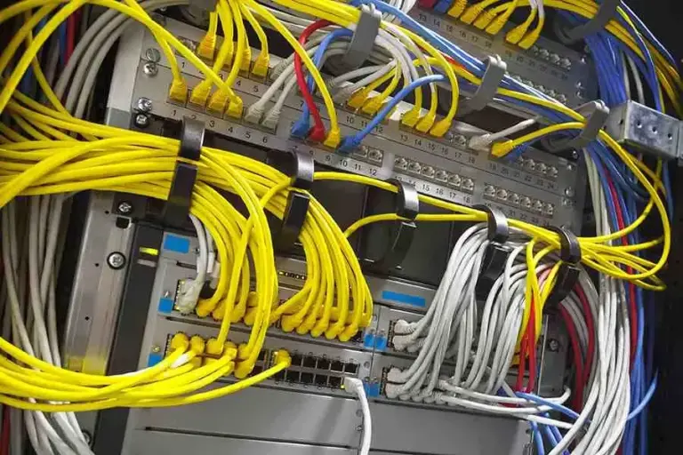 Network rack with yellow, white, blue and red patch cables routed between patch panels and switches