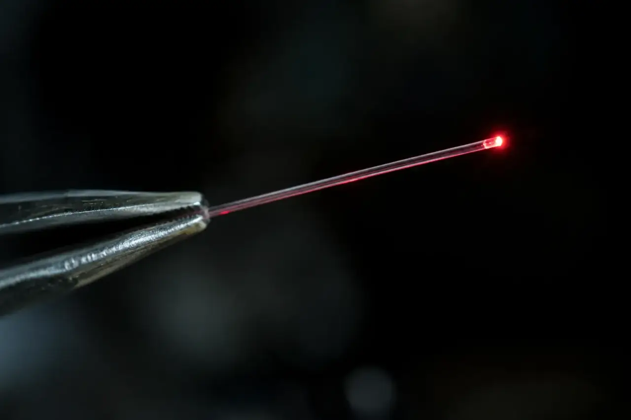 Single bare glass fiber held in tweezers with red light glowing at its tip