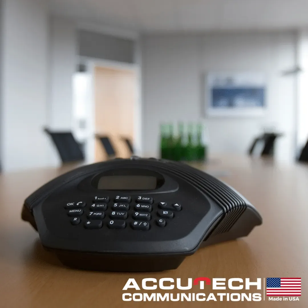 Black conference speakerphone with a keypad sitting on a boardroom table