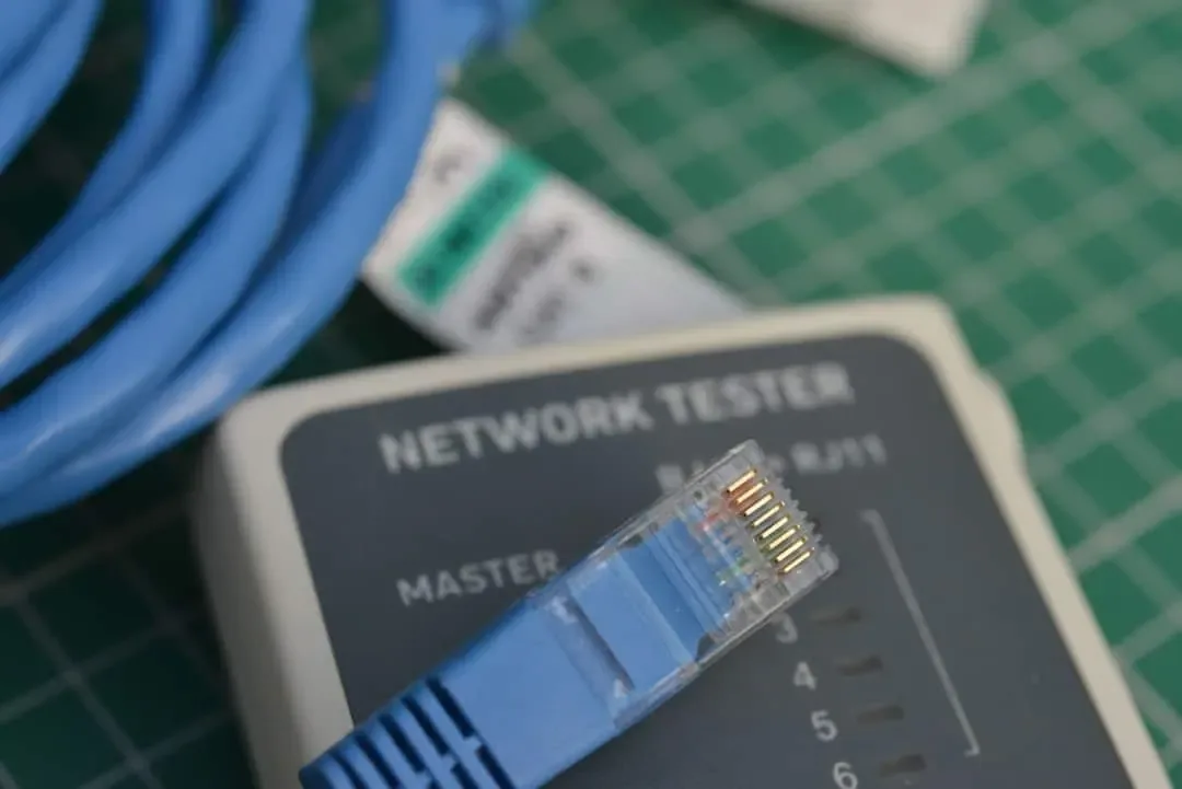 Blue RJ45 plug resting on a network cable tester with a coiled patch cord on a cutting mat