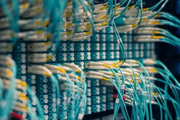 Dense rows of aqua fiber patch cords with yellow-tipped connectors in a fiber panel