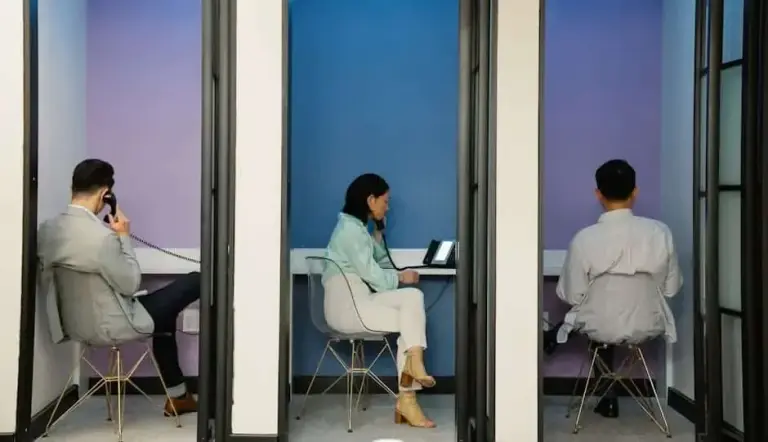 Three people in separate glass phone booths talking on corded desk phones