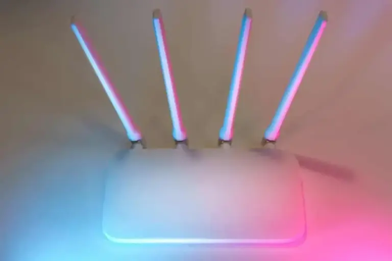 White wireless router with four antennas lit by pink and blue light