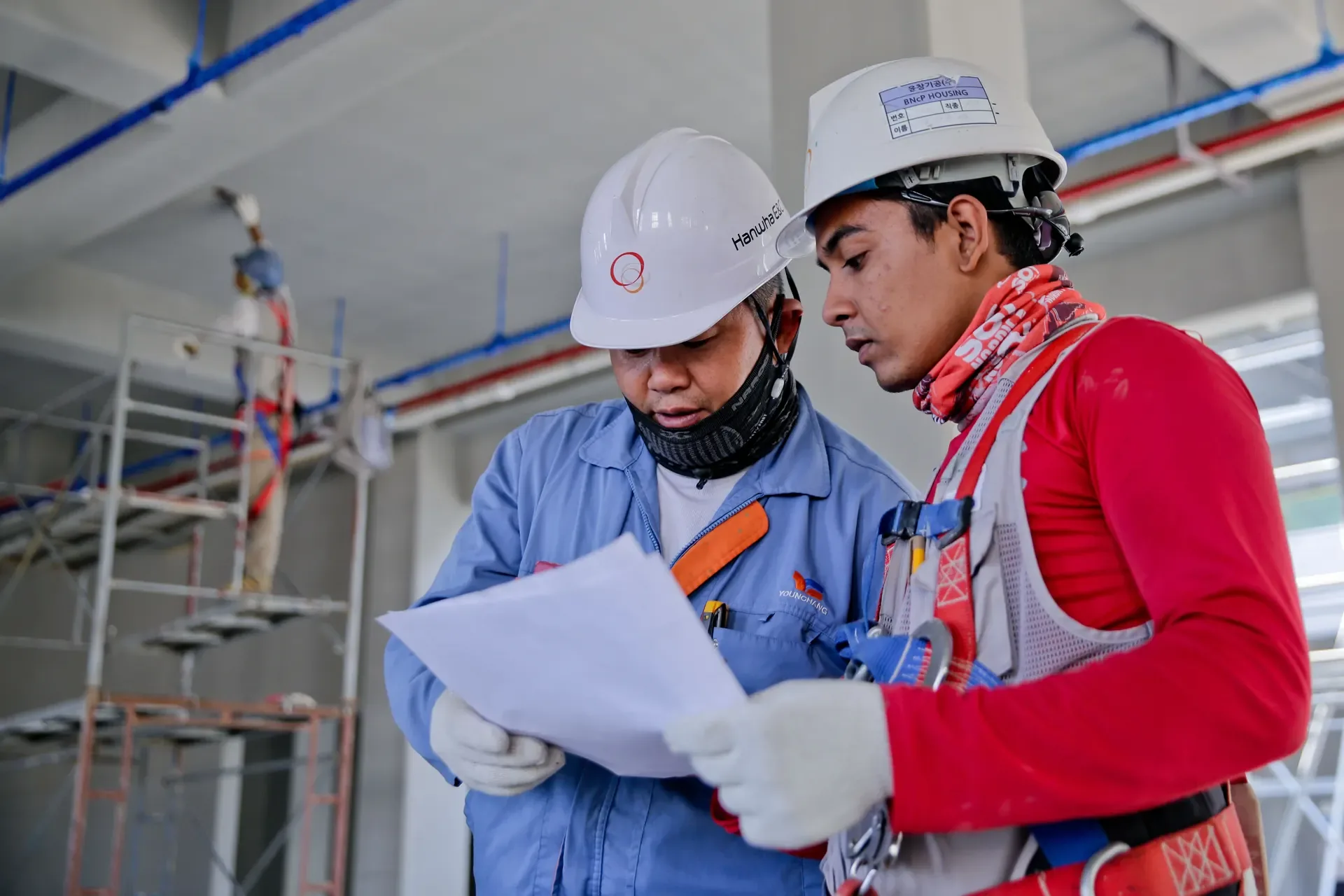 Two technicians in hard hats reviewing plans on a job site