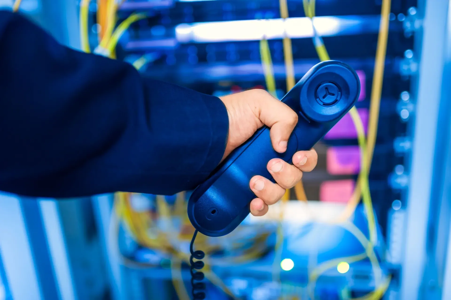 Hand holding a telephone handset in front of a network rack